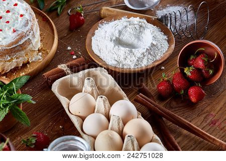 Top View Raw Ingredients For Cooking Strawberry Pie Or Cake On Wooden Table: Eggs, Flour, Sugar And 