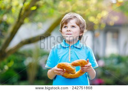 Adorable Little Kid Boy Eating Huge Big Bavarian German Pretzel. Happy Blond Child Enjoying Tasteful