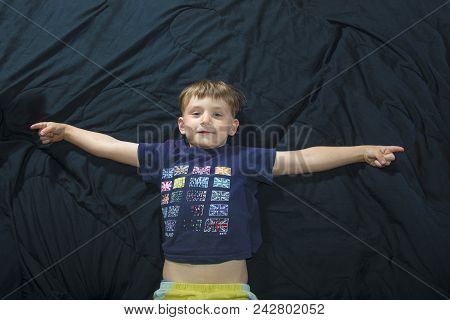 A Little Boy Is Lying On The Couch And Looks At The Camera And Raises His Hands To The Sides.