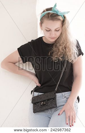 Girl Posing On A White Wall, With A Black Bag And A Bow On Her Head