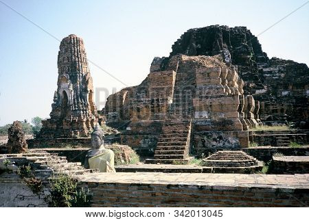 An Old Buddha Statue Sits Among The Ancient Ruins Of Wat Phra Mahathat In Ayutthaya, Thailand.