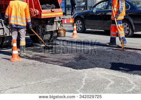 The Group Of Road Workers Is Repairing A Section Of The Carriageway With Fresh Asphalt.