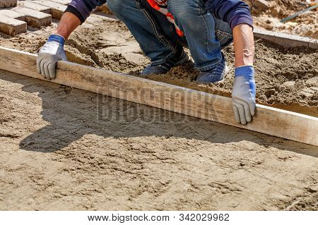 The Worker Cleans And Levels The Sand Base With A Wooden Board For Subsequent Smooth Laying Of Tiles