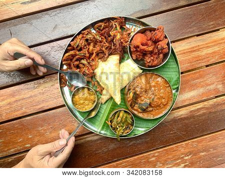 Man Using Fork And Spoon To Eat Banana Leaf Dish, Consists Of Fried Chicken, Curry Seafood, Lady Fin