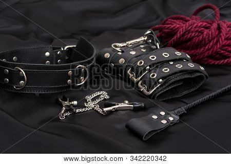 Leather Handcuffs, Shibari Rope, Nipple Clamps, Chain Collar And Stack On Black Background. Accessor