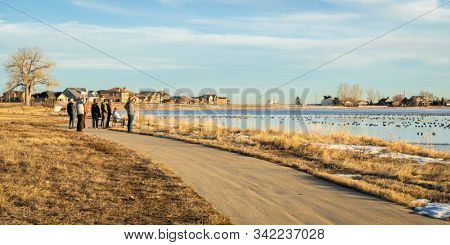 Windsor, CO, USA - December 24, 2019: Christmas holiday family walk, a group of older people on a recreational trail is watching migrating Canada geese on a partially frozen Windsor Lake in Colorado.
