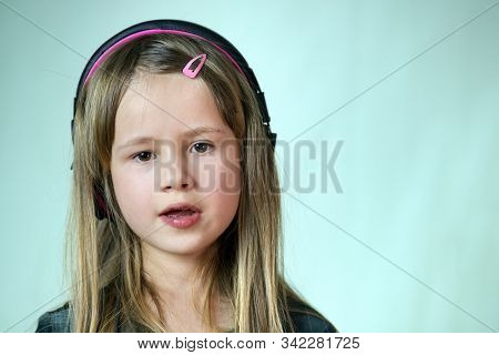 Pretty Smiling Cild Girl Listening To Music In Big Pink Earphones.