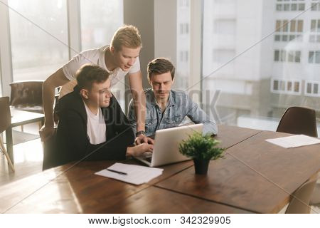Team Of Young Sturtupers Discussing Project Or Idea At The Table With Laptop In Company Meeting Room