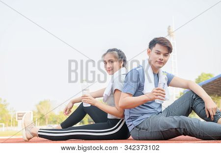 Portrait Of A Cute Hispanic Couple Holding Water And Resting After Runnng On Track At Studium, Healt