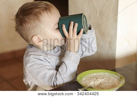Cute Caucasian Baby Boy With Blond Hairs Drinking Milk And Eating Porridge. Children Healthy Meal Co