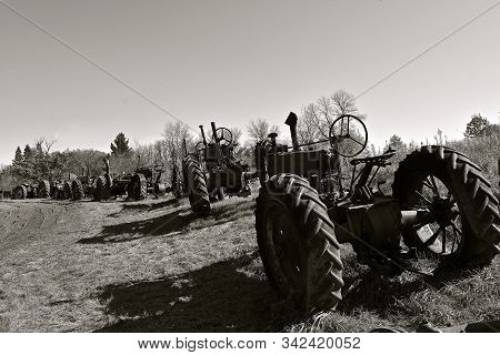 Old Unidentifiable Tractors Are Lined Up On A Rural Trail In A Country Setting. (black And White)