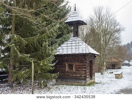 Old Wooden Belfry In Roznov Pod Radhostem. Just Snowing. Snow-covered Landscape.