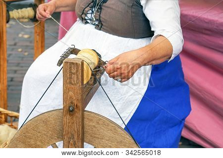 Craftswoman Using An Old Spinning Wheel To Turn Wool Into Yarn. Hands Of A Woman Demonstrating Tradi