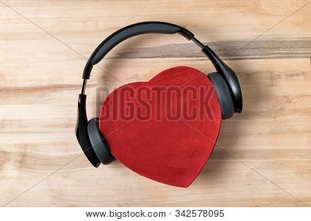 Full-size Wireless Headphones Pulled Over Red Heart-shaped Box On A Light Brown Wooden Table. Love M