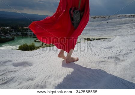 Young Barefoot Girl In Long Red Dress On White Travertines In Pamukkale And Looking To Wide Panorami