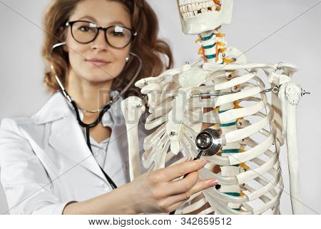 Woman In White Medical Gown. Doctor With Skeleton Layout On Gray Background. The Doctor In The Glass