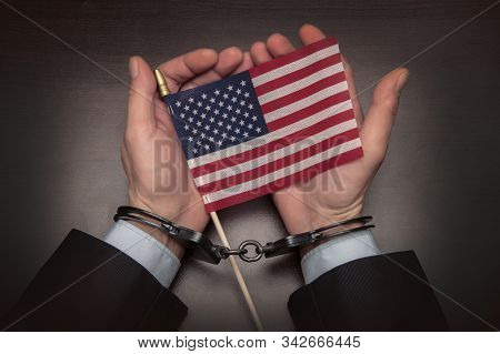 The Hands Of A Businessman In Handcuffs Holding An American Flag