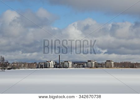 A Springlike And Sunny Day On A Snow Covered Lake. White Apartment Houses On The Other Side