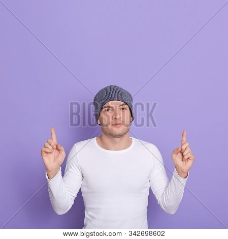Indoor Shot Of Serious Good Looking Man Making Gesture, Raising His Forefingers, Wearing Grey Hat An