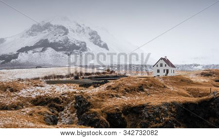 Lonely Beautiful House At The Small Fishing Village Of Arnarstapi And Mountain Cliff Covered In Snow