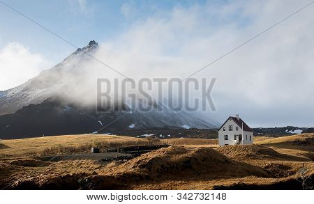 Lonely Beautiful House At The Small Fishing Village Of Arnarstapi And Mountain Cliff Covered In Snow