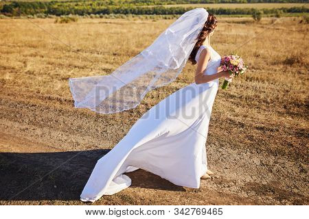 Beautiful Smiling Bride Wearing A Natural Flower Wreath And Standing In The Golden Summer Fields Wit