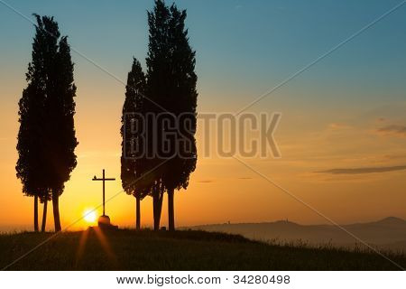 Mögött egy magányos kereszt között fák ciprusok, a dombos Toszkána közelében Pienza Ital a Sunrise