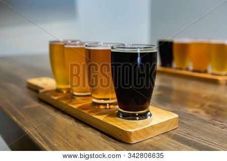 Flight Of Craft Four Of Different Beers Glasses With Black Beer On A Wooden Tray. During A Tasting S