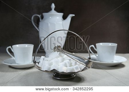 Sugar Cubes In Metal Vintage Sugar  Bowl With Sugar Tongs And Cups With Coffee Or Tea Pot.