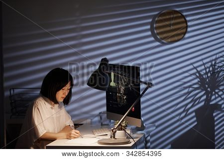 Asian Young Businesswoman Writing At Her Workplace In Front Of Computer Monitor She Working Till Lat