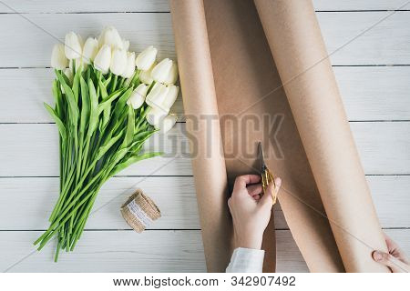 Woman Florist Wrapping Beautiful Bouquet Of White Tulips In Pack Craft Paper On The Wooden Table. Fl