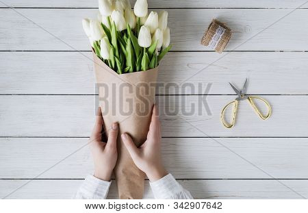Woman Florist Wrapping Beautiful Bouquet Of White Tulips In Pack Craft Paper On The Wooden Table. Fl