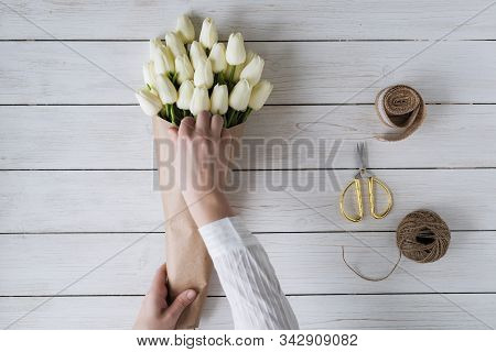 Woman Florist Wrapping Beautiful Bouquet Of White Tulips In Pack Craft Paper On The Wooden Table. Fl