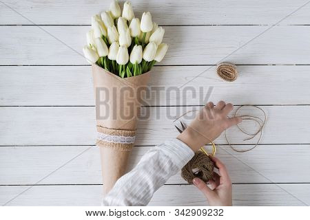 Woman Florist Wrapping Beautiful Bouquet Of White Tulips In Pack Craft Paper On The Wooden Table. Fl