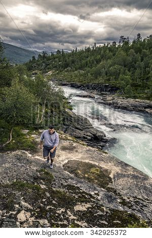 Young Man Walking Along The Mountanious River, Norway