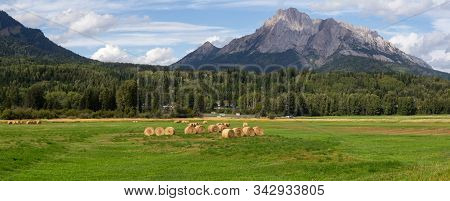 Bales Of Hay In A Farm Field With Canadian Rocky Mountains In The Background During A Vibrant Sunny 