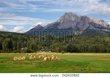 Bales Of Hay In A Farm Field With Canadian Rocky Mountains In The Background During A Vibrant Sunny 