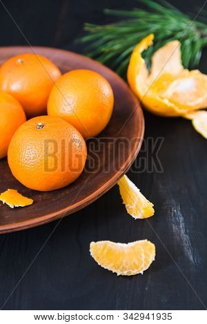 Fresh Whole And Peeled Tangerines Lie On An Old Clay Plate On A Dark Background