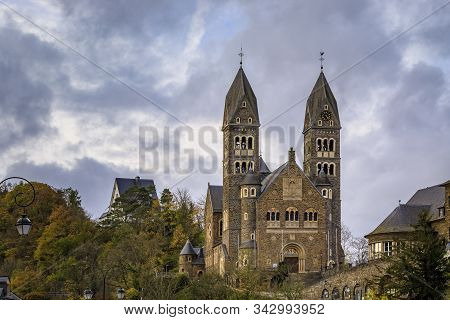 Stone facade of the neo romanesque Roman Catholic Church of Saints Come and Damien in Clervaux, Luxembourg surrounded by a forest in the fall