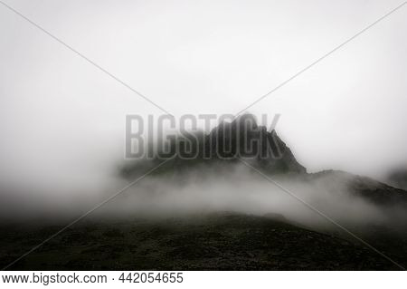 Overcast Alpine View With Mountain Silhouette Fragments Through Fog And Clouds