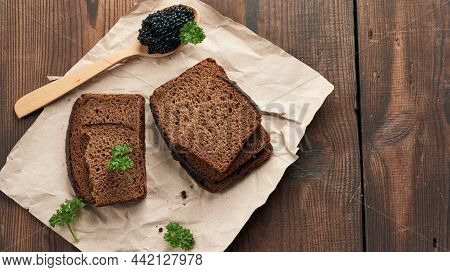 Fresh Grainy Black Paddlefish Caviar In Brown Wooden Spoon On A Brown Table, Top View