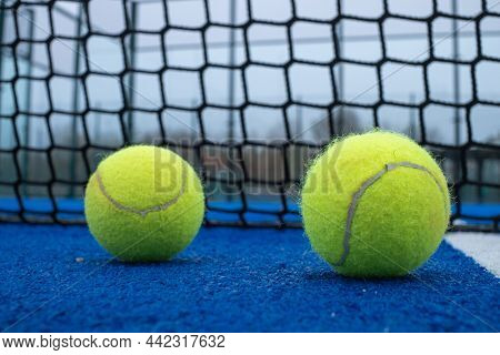 Selective Focus. Two Paddle Tennis Balls On A Blue Court With The Net Out Of Focus In The Background