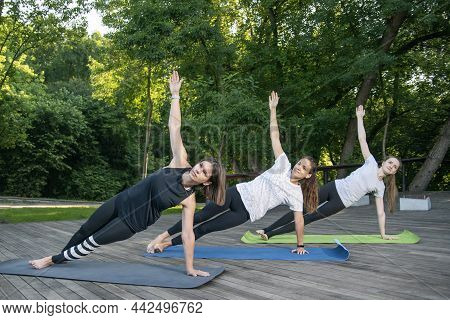 Group Of Young Women Practice Yoga Early In The Morning Outdoors. Side Plank. Vasishthasana