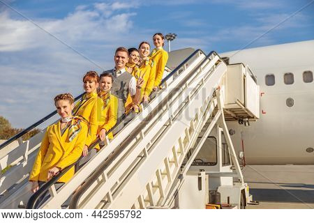 Cheerful Aircrew Standing On Airplane Stairs Under Blue Sky
