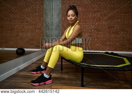 Attractive Young Woman With Slim Body And Flat Belly In Bright Yellow Tracksuit Sitting On A Trampol