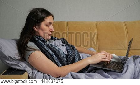 Sick Brunette Woman With Runny Nose Wrapped In Scarf Works Distantly Via Laptop Sitting Under Warm B