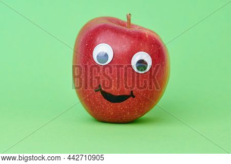 Red Apple With A Funny Lauging Face On Green Background