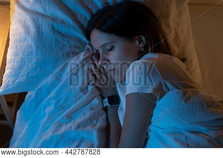 Top View Of A Beautiful Girl Sleeping Cozily On A Bed In Her Night Room With Blue Colors From The Mo