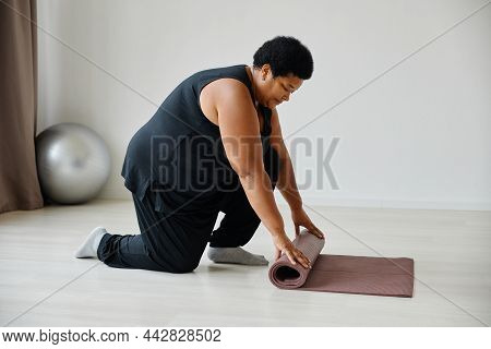 Side View Portrait Of Black Senior Woman Unrolling Yoga Mat While Exercising In Studio, Copy Space
