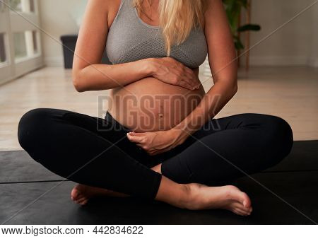 Pregnant Caucasian Female Holding Her Belly While Sitting On Yoga Mat At Home. Health And Wellness